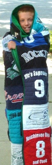 A boy wrapped up in his baseball quilt.