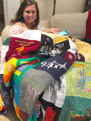 A girl sitting on a couch under her T-shirt quilt.
